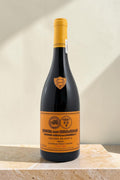 Botella de vino tinto Wellnex Gran Reserva con etiqueta naranja y cápsula amarilla sobre superficie de piedra