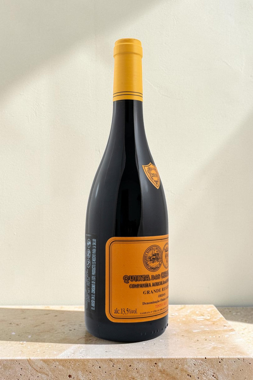 Botella de vino tinto Wellnex Gran Reserva con etiqueta amarilla sobre superficie de piedra clara