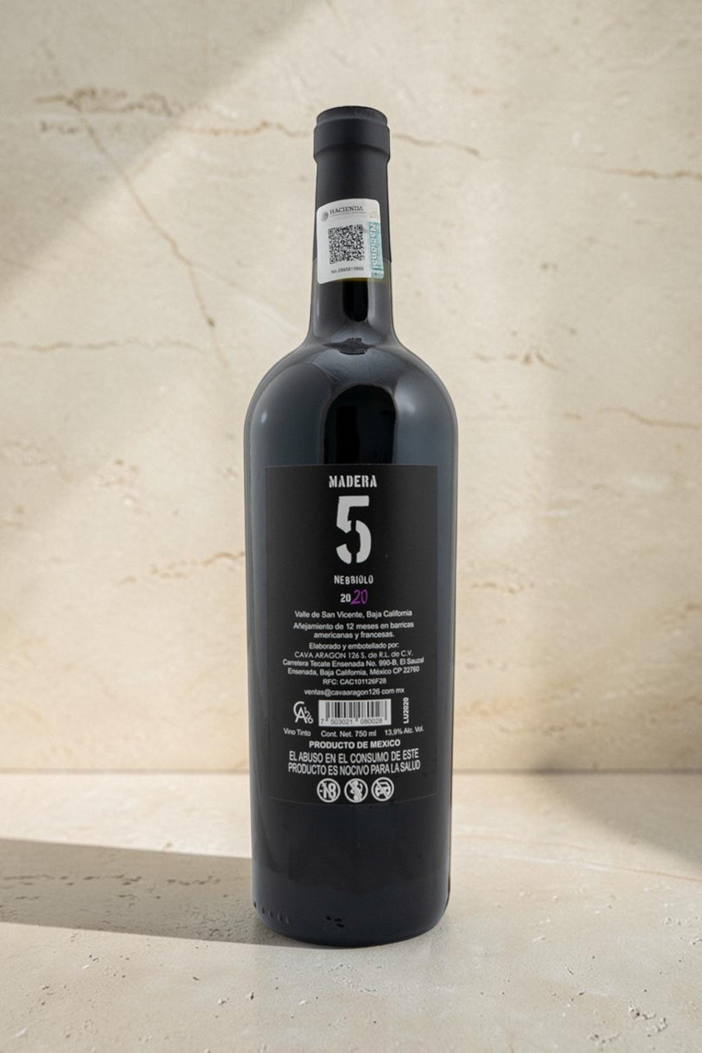 Botella de vino tinto Wellnex Nebbiolo Madra 5 con etiqueta trasera detallada sobre fondo de piedra clara