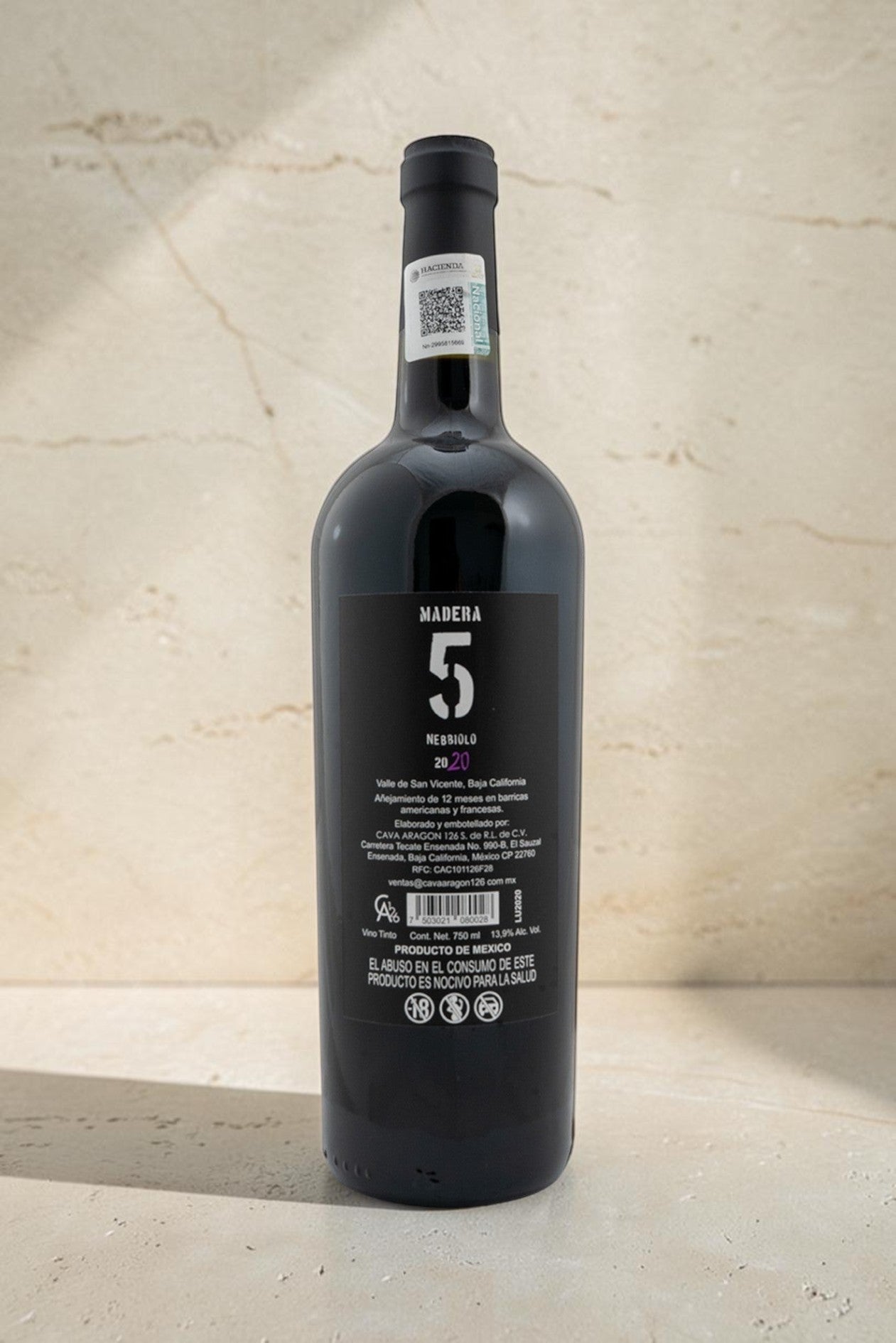 Botella de vino tinto Wellnex Nebbiolo Madra 5 con etiqueta trasera detallada sobre fondo de piedra clara