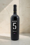 Botella de vino tinto Wellnex Nebbiolo Madra 5 con etiqueta negra y número 5 grande sobre fondo de piedra claro