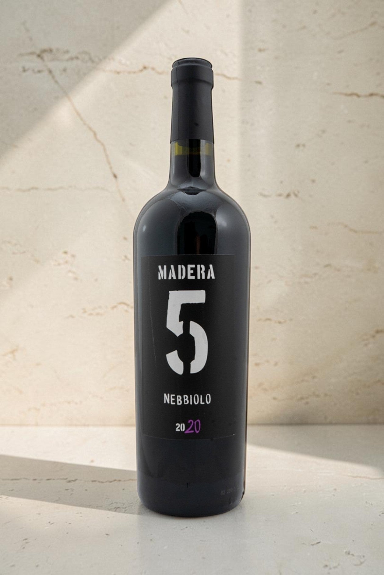 Botella de vino tinto Wellnex Nebbiolo Madra 5 con etiqueta negra y número 5 grande sobre fondo de piedra claro
