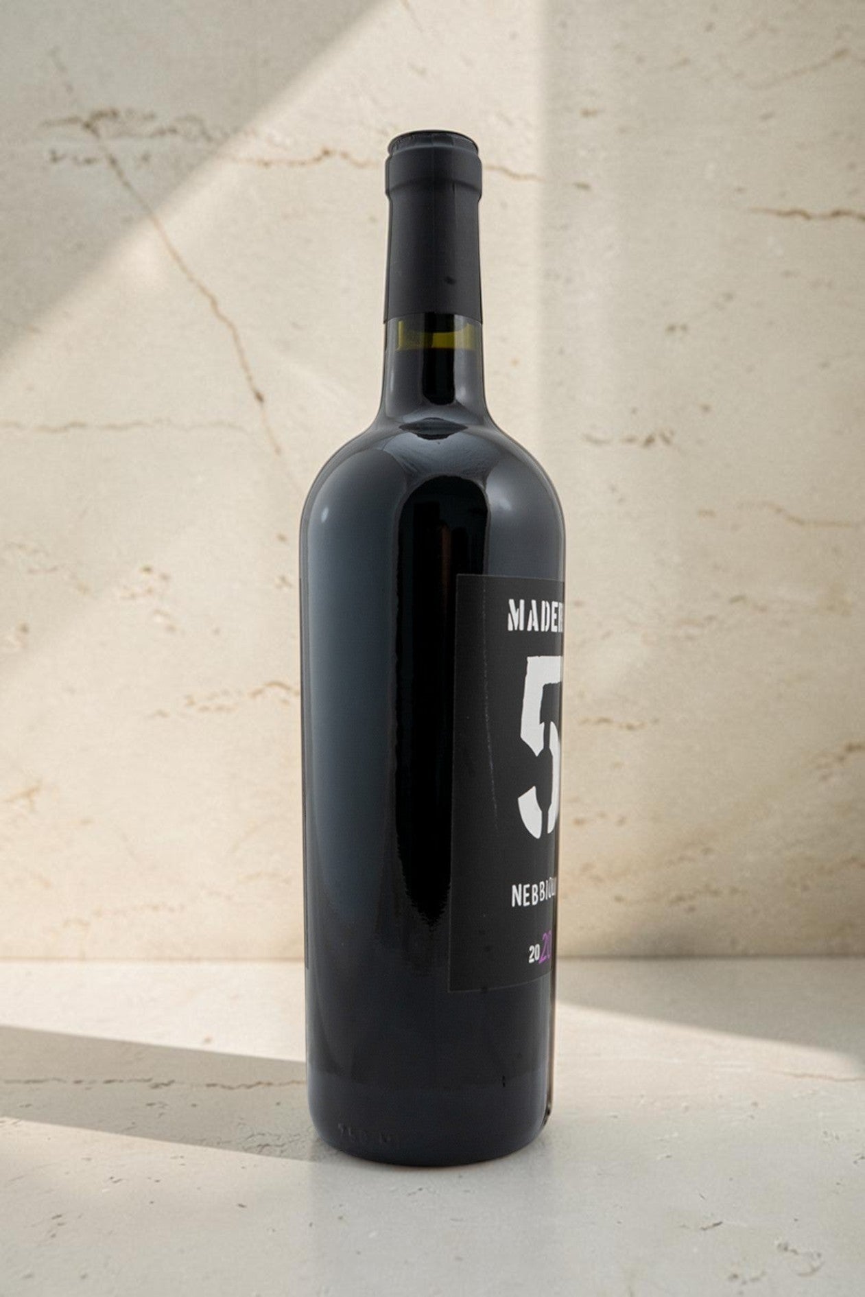 Botella de vino tinto Wellnex Nebbiolo Madra 5 de color rubí profundo con etiqueta moderna sobre fondo de piedra