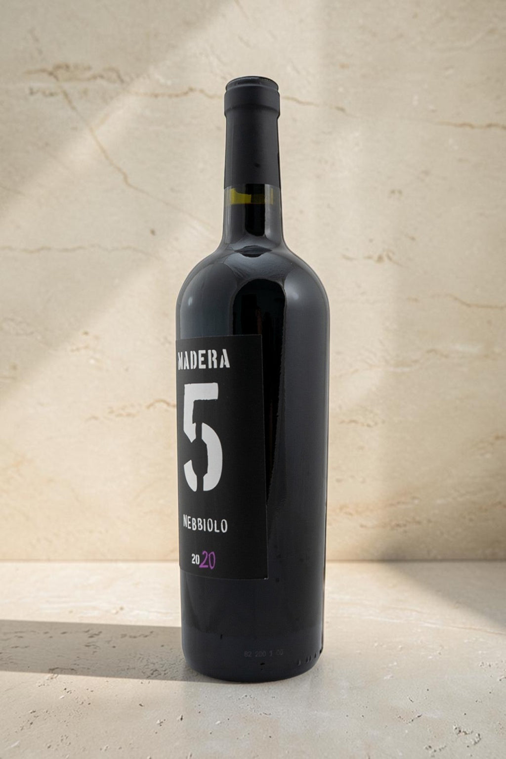 Botella de vino tinto Wellnex Nebbiolo Madra 5 con etiqueta negra moderna sobre fondo de piedra beige