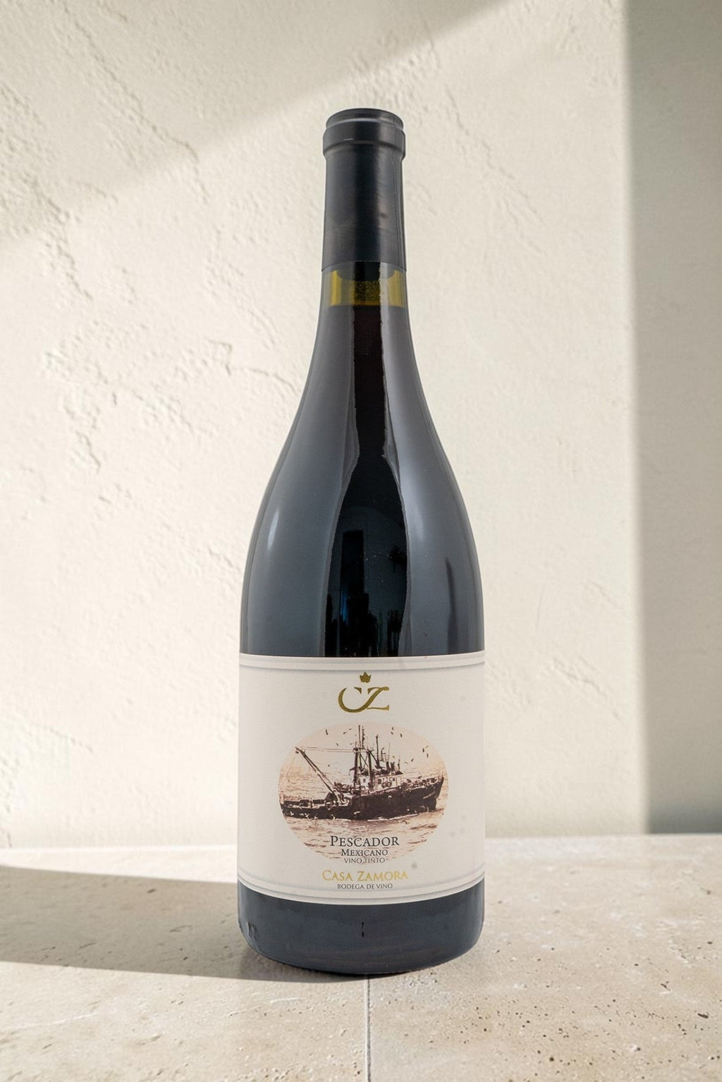 Botella de vino tinto Pescador de Wellnex con etiqueta ilustrada de un barco pesquero sobre fondo texturizado claro