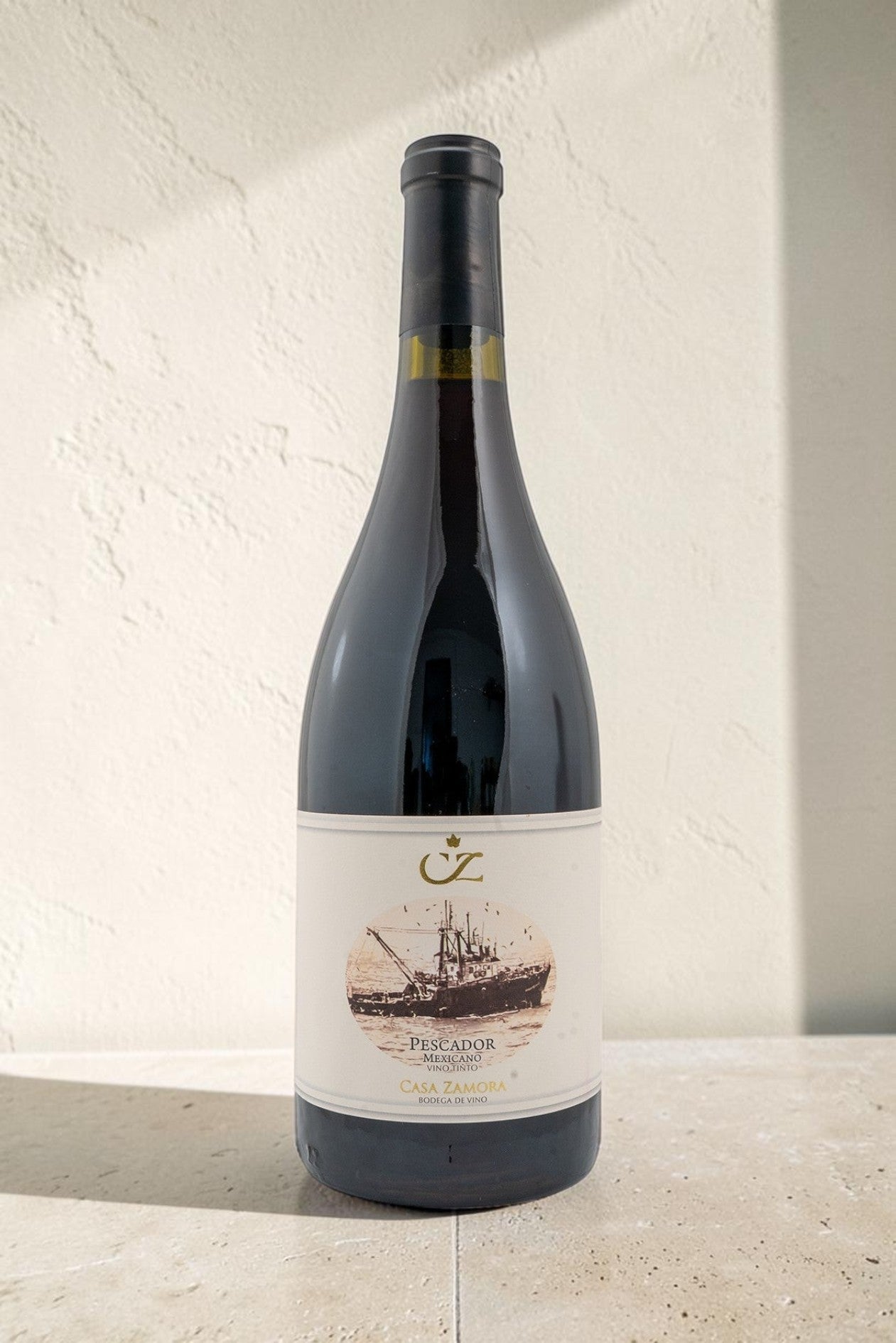Botella de vino tinto Pescador de Wellnex con etiqueta ilustrada de un barco pesquero sobre fondo texturizado claro