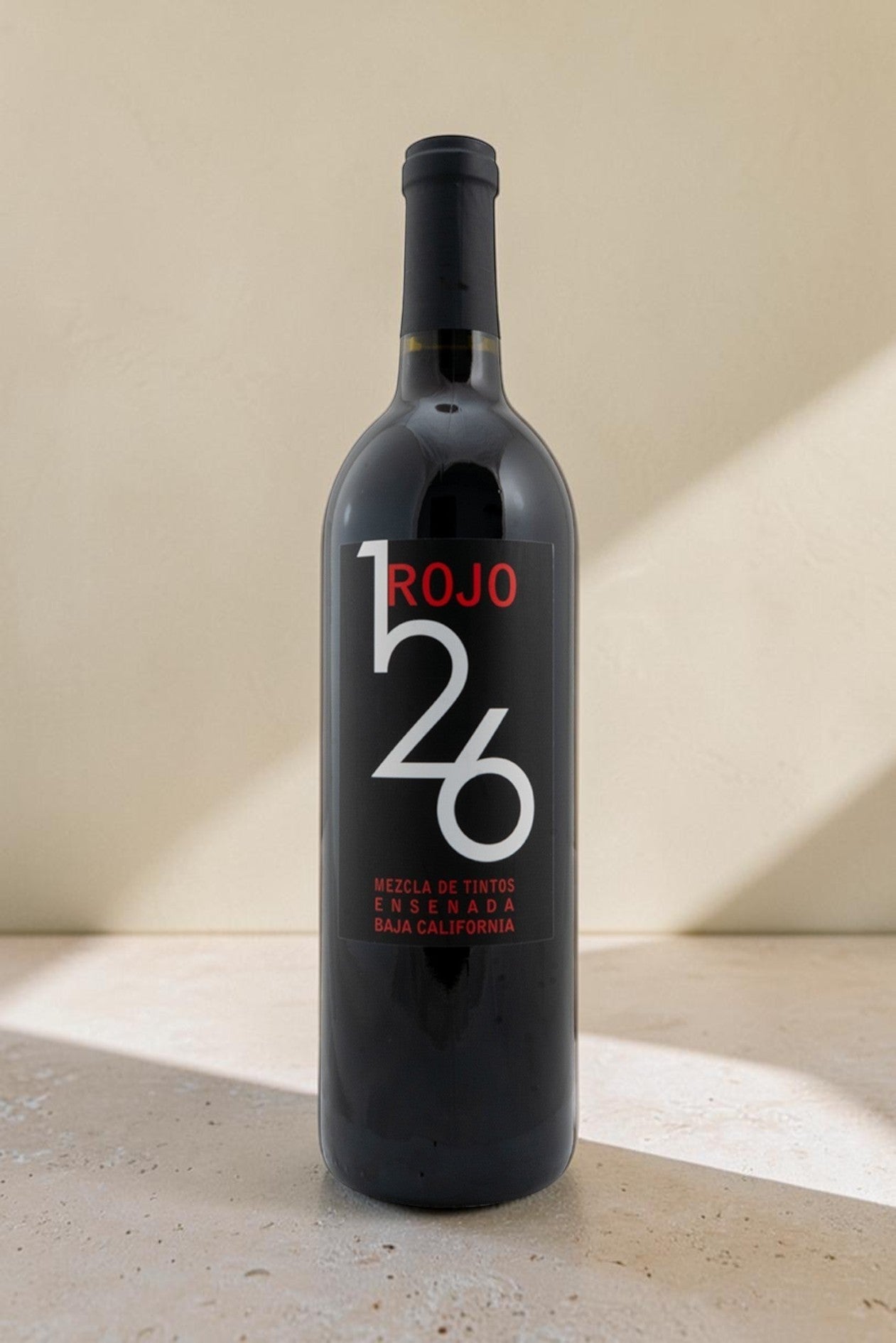 Botella de vino tinto Wellnex Rojo 126 con etiqueta negra moderna sobre superficie de piedra clara