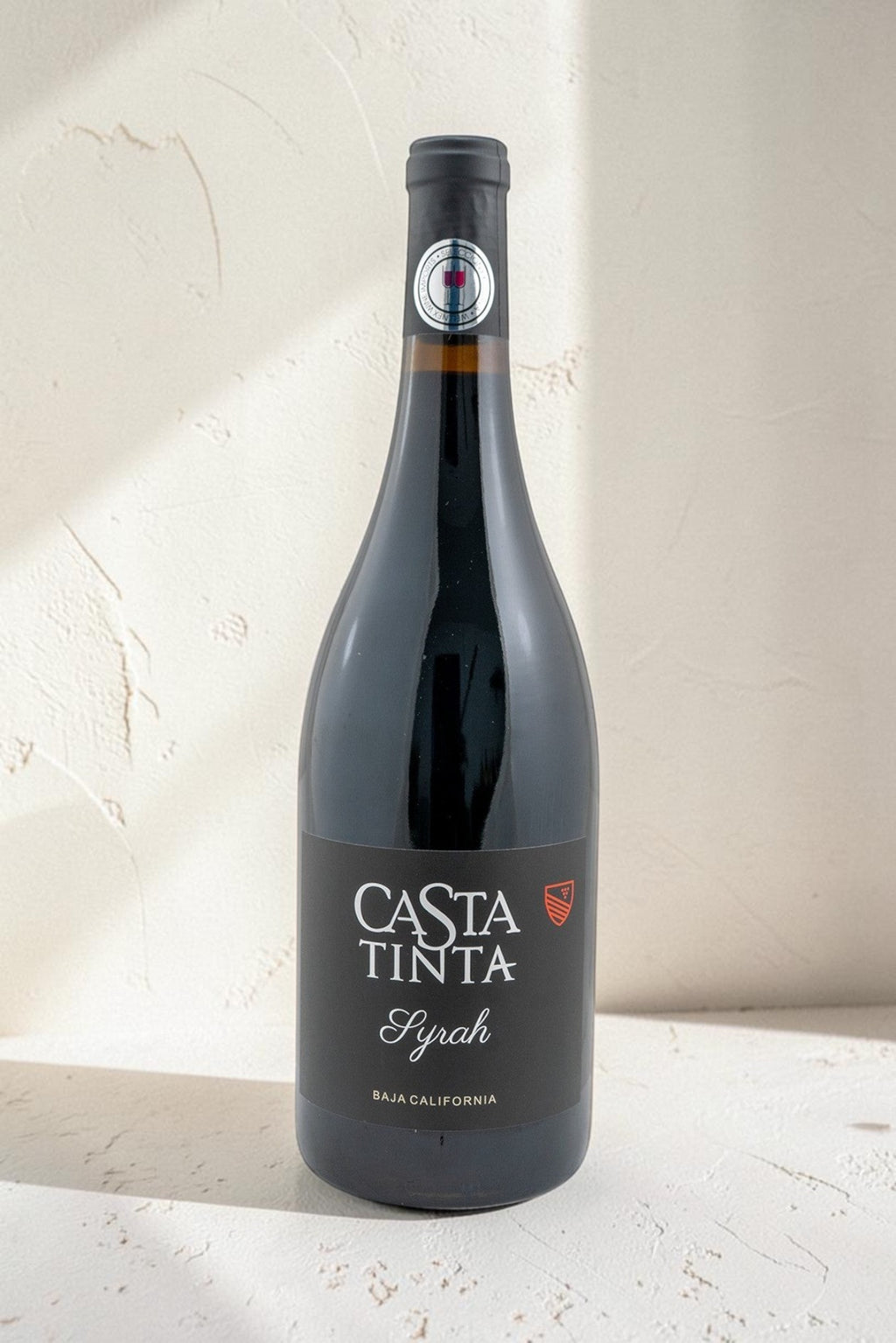 Botella de vino tinto Syrah Casta Tinta de Wellnex con etiqueta negra elegante sobre fondo texturizado claro