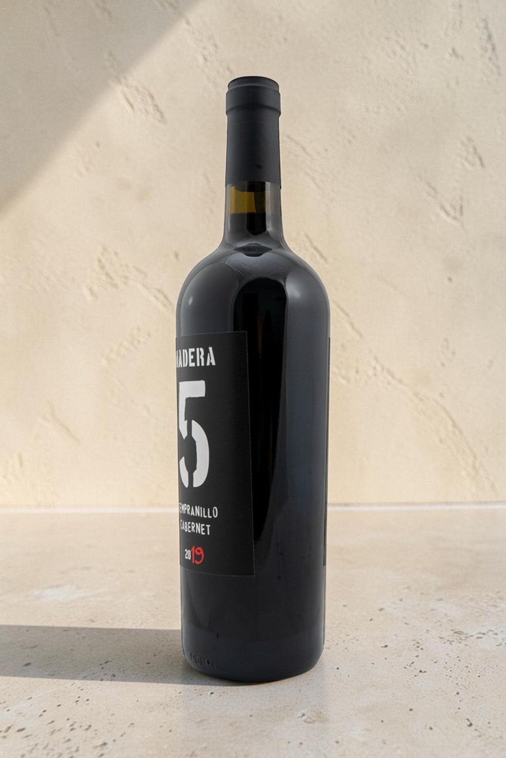 Botella de vino tinto Wellnex Tempranillo Cabernet con etiqueta negra moderna sobre fondo de piedra clara